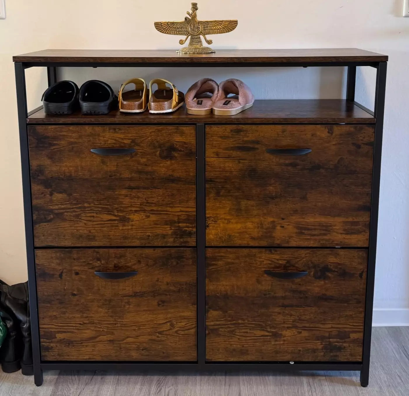 Wooden shoe cabinet with shoes on top against a white wall
