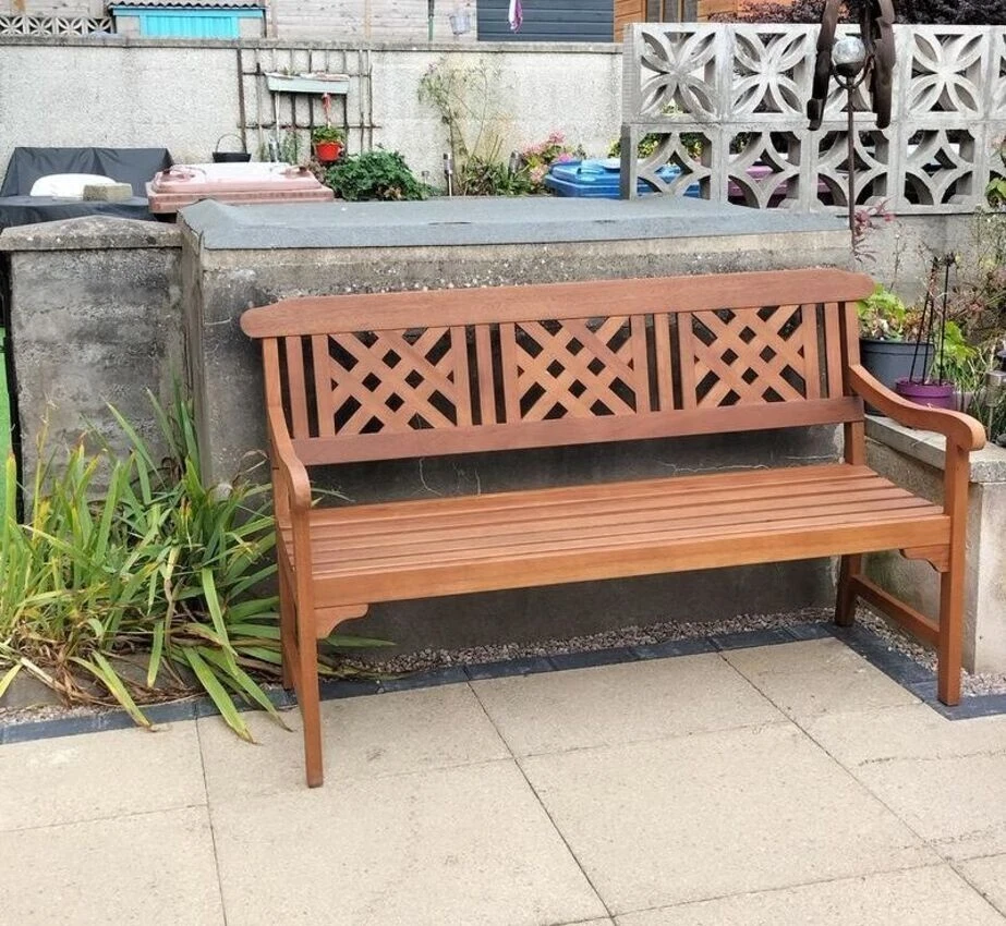 Wooden bench with lattice backrest on a patio area with plants and a wall in the background