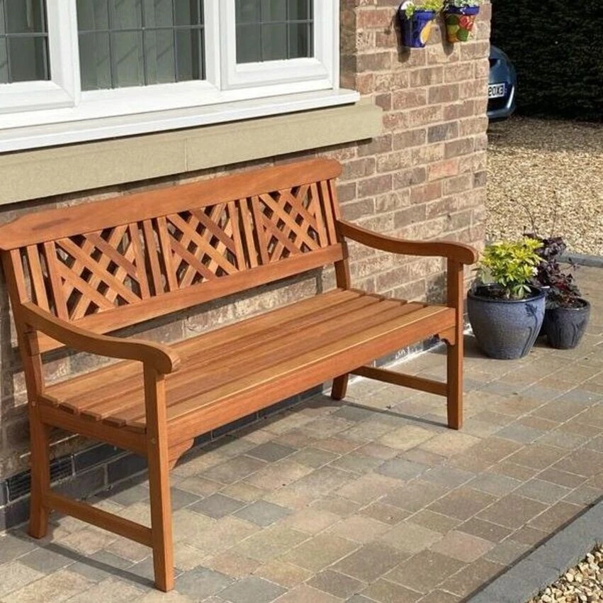 Wooden bench with lattice backrest on a patio next to a brick wall.